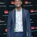 An individual stands for a portrait at the Alpha Omega Alpha 2023 Induction Ceremony at UTMB, wearing green honor cords in front of a UTMB Health and John Sealy School of Medicine logo backdrop.