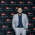 An individual stands for a portrait at the Alpha Omega Alpha 2023 Induction Ceremony at UTMB in front of a UTMB Health and John Sealy School of Medicine branded backdrop.