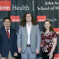 Three individuals stand together at the Alpha Omega Alpha 2023 Induction Ceremony at UTMB, posing in front of a UTMB Health and John Sealy School of Medicine logo backdrop.
