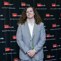 An individual poses for a portrait at the Alpha Omega Alpha 2023 Induction Ceremony at UTMB in front of a UTMB Health and John Sealy School of Medicine branded backdrop.