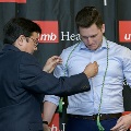 An individual places honor cords around another individual’s neck during the Alpha Omega Alpha 2023 Induction Ceremony at UTMB, with a UTMB Health backdrop visible behind them.