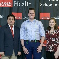 Three individuals stand together at the Alpha Omega Alpha 2023 Induction Ceremony at UTMB, posing in front of a UTMB Health and John Sealy School of Medicine logo backdrop.