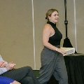 An individual walks through a ballroom holding a program during the Alpha Omega Alpha 2023 Induction Ceremony at UTMB, with seated attendees visible to the side.