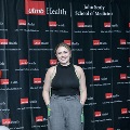 An individual stands centered between red, white, and gray balloon columns at the Alpha Omega Alpha 2023 Induction Ceremony at UTMB, wearing honor cords in front of a UTMB Health and John Sealy School of Medicine backdrop.