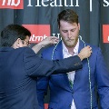 An individual places honor cords around another individual’s neck during the Alpha Omega Alpha 2023 Induction Ceremony at UTMB, with a UTMB Health and John Sealy School of Medicine backdrop behind them.