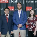 Three individuals stand together at the Alpha Omega Alpha 2023 Induction Ceremony at UTMB, posing in front of a UTMB Health and John Sealy School of Medicine logo backdrop.