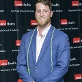 An individual poses in front of a UTMB Health and John Sealy School of Medicine branded backdrop during the Alpha Omega Alpha 2023 Induction Ceremony, wearing honor cords and a blue blazer.