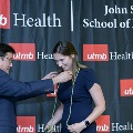 An individual places honor cords around another individual’s neck during the Alpha Omega Alpha 2023 Induction Ceremony at UTMB, with a branded UTMB Health backdrop visible behind.
