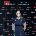 An individual stands in front of a UTMB Health and John Sealy School of Medicine branded backdrop wearing honor cords during the Alpha Omega Alpha 2023 Induction Ceremony.