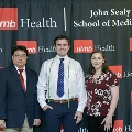 Three individuals stand together at the Alpha Omega Alpha 2023 Induction Ceremony at UTMB, posing in front of a UTMB Health and John Sealy School of Medicine branded backdrop.