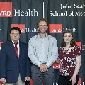 Three individuals stand together at the Alpha Omega Alpha 2023 Induction Ceremony at UTMB, posing in front of a UTMB Health and John Sealy School of Medicine branded backdrop.