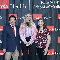 Three individuals pose together at the Alpha Omega Alpha 2023 Induction Ceremony at UTMB in front of a UTMB Health and John Sealy School of Medicine logo backdrop.