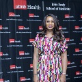 An individual poses at the Alpha Omega Alpha 2023 Induction Ceremony at UTMB, standing between red, white, and gray balloon columns in front of a UTMB Health and John Sealy School of Medicine backdrop.