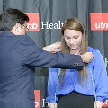 An individual places honor cords around another individual’s neck during the Alpha Omega Alpha 2023 Induction Ceremony at UTMB, with a UTMB Health and John Sealy School of Medicine logo backdrop behind them.