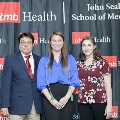 Three individuals stand together at the Alpha Omega Alpha 2023 Induction Ceremony at UTMB, posing in front of a UTMB Health and John Sealy School of Medicine logo backdrop.