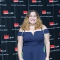 An individual stands for a portrait at the Alpha Omega Alpha 2023 Induction Ceremony at UTMB, in front of a UTMB Health and John Sealy School of Medicine logo backdrop.