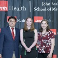 Three individuals stand together at the Alpha Omega Alpha 2023 Induction Ceremony at UTMB, posing in front of a UTMB Health and John Sealy School of Medicine logo backdrop.