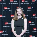 An individual stands for a portrait at the Alpha Omega Alpha 2023 Induction Ceremony at UTMB in front of a UTMB Health and John Sealy School of Medicine branded backdrop.