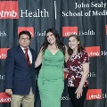 Three individuals pose together at the Alpha Omega Alpha 2023 Induction Ceremony at UTMB in front of a UTMB Health and John Sealy School of Medicine logo backdrop.