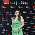 An individual poses in front of a UTMB Health and John Sealy School of Medicine backdrop, framed by red, white, and gray balloon columns, holding honor cords during the Alpha Omega Alpha 2023 Induction Ceremony.