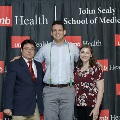 Three individuals stand together at the Alpha Omega Alpha 2023 Induction Ceremony at UTMB in front of a UTMB Health and John Sealy School of Medicine branded backdrop.