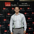 An individual poses in front of a UTMB Health and John Sealy School of Medicine branded backdrop with red, white, and gray balloon columns while wearing honor cords during the Alpha Omega Alpha 2023 Induction Ceremony.