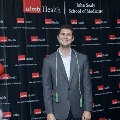 An individual stands in front of a UTMB Health and John Sealy School of Medicine backdrop, framed by red, white, and gray balloon columns, wearing honor cords at the Alpha Omega Alpha 2023 Induction Ceremony.