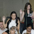 Attendees stand among seated guests, raising one hand and reading from printed programs during the Alpha Omega Alpha 2023 Induction Ceremony at UTMB in a ballroom setting.