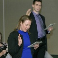 Individuals stand and raise one hand while reading from printed programs during the Alpha Omega Alpha 2023 Induction Ceremony at UTMB, participating in an oath recitation in a ballroom setting.