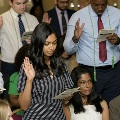 Attendees stand closely together raising one hand and reading from printed programs during the Alpha Omega Alpha 2023 Induction Ceremony at UTMB, with seated participants visible in the foreground.