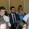 Several inductees stand among seated attendees, raising one hand and reading from programs during the Alpha Omega Alpha 2023 Induction Ceremony at UTMB as part of the oath-taking portion.