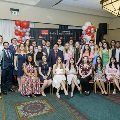 A large group of attendees pose together at the Alpha Omega Alpha 2023 Induction Ceremony at UTMB, arranged in seated and standing rows in front of a UTMB Health backdrop with balloon decorations.