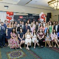 A large group of inductees and guests pose together in rows at the Alpha Omega Alpha 2023 Induction Ceremony at UTMB, with a UTMB Health and John Sealy School of Medicine backdrop and red, white, and gray balloon columns.