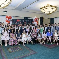 A large group of inductees and guests sit and stand in rows for a formal photo at the Alpha Omega Alpha 2023 Induction Ceremony at UTMB, with a UTMB Health and John Sealy School of Medicine backdrop and balloon columns.