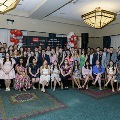 A large group of attendees sit and stand together for a formal group photo at the Alpha Omega Alpha 2023 Induction Ceremony at UTMB in a ballroom with chandeliers and a UTMB backdrop.
