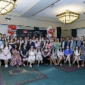A large group of inductees and guests pose together at the Alpha Omega Alpha 2023 Induction Ceremony at UTMB, arranged in rows in a ballroom with chandeliers and a UTMB Health backdrop.