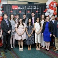 A group of individuals pose together at the Alpha Omega Alpha 2023 Induction Ceremony at UTMB, standing in front of a UTMB Health and John Sealy School of Medicine backdrop with balloon columns on both sides.