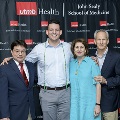 Four individuals pose together at the Alpha Omega Alpha 2023 Induction Ceremony at UTMB, standing in front of a UTMB Health and John Sealy School of Medicine backdrop framed by red, white, and gray balloon columns.