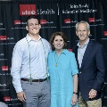 Three individuals stand together at the Alpha Omega Alpha 2023 Induction Ceremony at UTMB in front of a UTMB Health and John Sealy School of Medicine logo backdrop with balloon decorations at the sides.