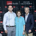 Three individuals pose together at the Alpha Omega Alpha 2023 Induction Ceremony at UTMB, standing in front of a UTMB Health backdrop with red, white, and gray balloon columns on either side.
