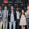 Six individuals pose together at the Alpha Omega Alpha 2023 Induction Ceremony at UTMB, standing in front of a UTMB Health and John Sealy School of Medicine backdrop framed by red, white, and gray balloon columns.