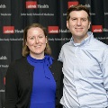 Two individuals pose together at the Alpha Omega Alpha 2023 Induction Ceremony at UTMB, standing in front of a black backdrop displaying UTMB Health and John Sealy School of Medicine logos.