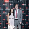 Two individuals pose for a full-length photo at the Alpha Omega Alpha 2023 Induction Ceremony at UTMB, framed by red and white balloon columns and a UTMB Health backdrop.