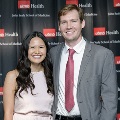 Two individuals stand side by side at the Alpha Omega Alpha 2023 Induction Ceremony at UTMB, posing in front of a UTMB Health and John Sealy School of Medicine logo backdrop.