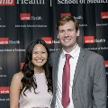 Two individuals pose together at the Alpha Omega Alpha 2023 Induction Ceremony at UTMB, standing in front of a black backdrop displaying UTMB Health and John Sealy School of Medicine logos.