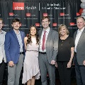 A group of six individuals stand together at the Alpha Omega Alpha 2023 Induction Ceremony at UTMB, posing in front of a UTMB Health backdrop framed by red and white balloon columns.