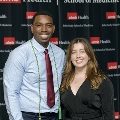 Two individuals pose together at the Alpha Omega Alpha 2023 Induction Ceremony at UTMB in front of a UTMB Health and John Sealy School of Medicine logo backdrop.