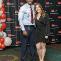 Two individuals pose together at the Alpha Omega Alpha 2023 Induction Ceremony at UTMB, standing in front of a UTMB Health and John Sealy School of Medicine backdrop with red and white balloon decorations visible.