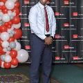 An individual stands for a full-length portrait at the Alpha Omega Alpha 2023 Induction Ceremony at UTMB, posed beside a red, white, and gray balloon display with a UTMB Health backdrop behind.