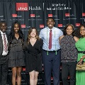 A group of individuals pose together at the Alpha Omega Alpha 2023 Induction Ceremony at UTMB in front of a UTMB Health and John Sealy School of Medicine backdrop framed by red and white balloon columns.